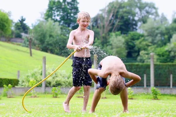 Dva šťastné kluci hrají na zahradě s zavlažovací hadice — Stock fotografie