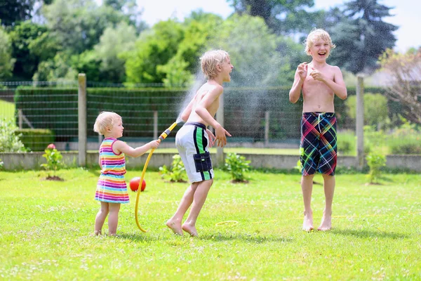 Grupp av glada barn som leker i trädgården med vattning slang — Stockfoto