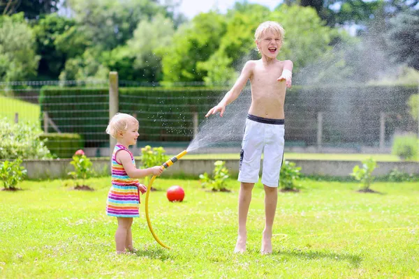 Bratr a sestra hraje v zahradě s zavlažovací hadice — Stock fotografie