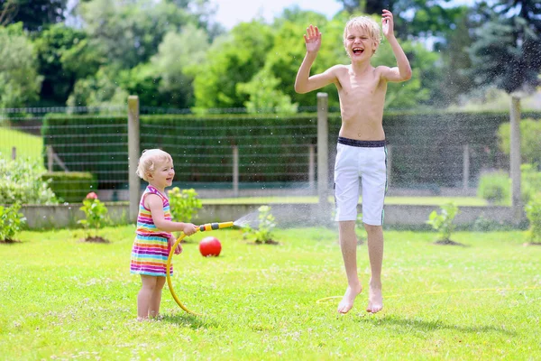 Hermano y hermana jugando en el jardín con manguera de riego —  Fotos de Stock