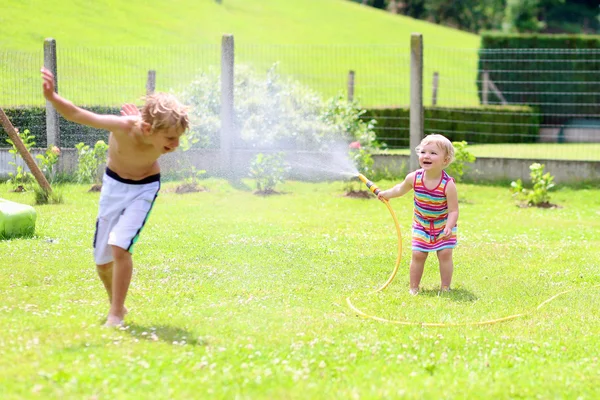 Брат и сестра играют в саду из поливающего шланга — стоковое фото
