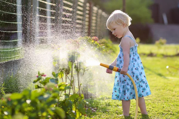 Schattig klein meisje drenken bloemen in de tuin met behulp van spray slang — Stockfoto