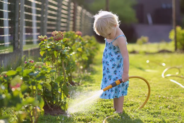 Linda niña regando flores en el jardín usando manguera de pulverización —  Fotos de Stock