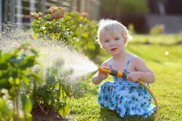 Linda niña regando flores en el jardín usando manguera de pulverización —  Fotos de Stock