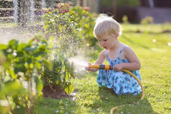 Söt liten flicka vattna blommorna i trädgården med sugslang — Stockfoto