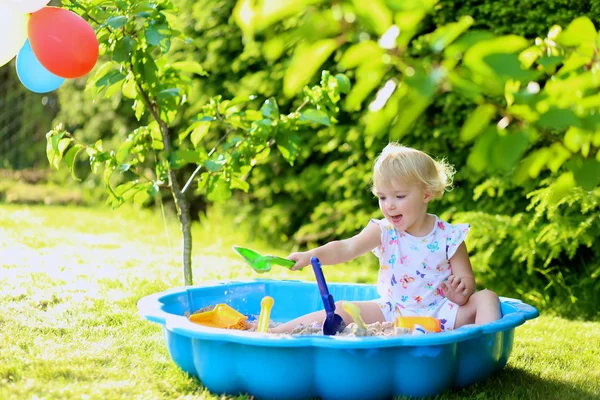 Счастливая маленькая девочка играет с песком в солнечном саду — стоковое фото