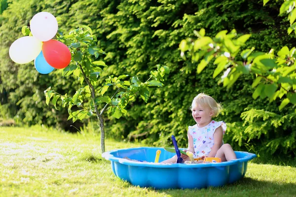 Boldog kis lány játszik a homok, napfényes kertben — Stock Fotó