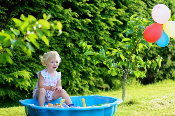 Šťastná holčička hraje s pískem v slunné zahradě — Stock fotografie