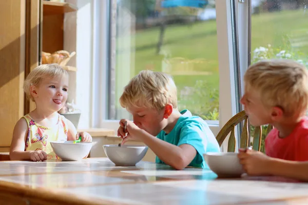 Grupo de niños felices desayunando saludables sentados en una cocina soleada —  Fotos de Stock