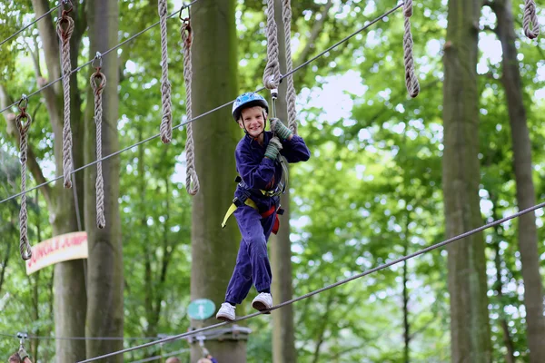 Lindo chico de escuela disfrutando de un día soleado en un parque de actividades de aventura de escalada — Foto de Stock