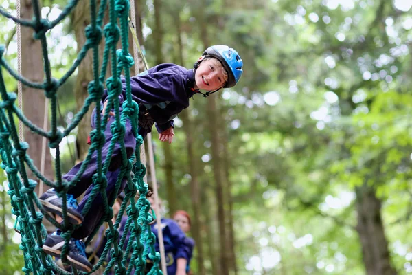 Leuke schooljongen geniet van een zonnige dag in een klimavontuur activiteitenpark — Stockfoto