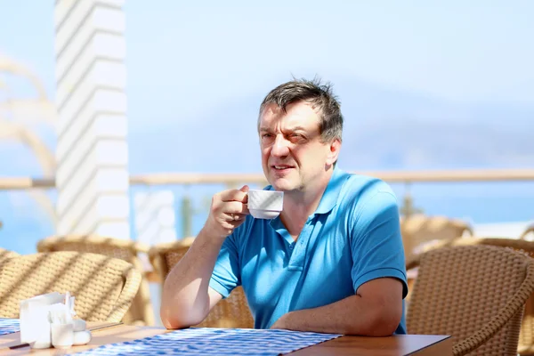 Hombre guapo bebiendo café sentado en acogedora cafetería de playa — Foto de Stock