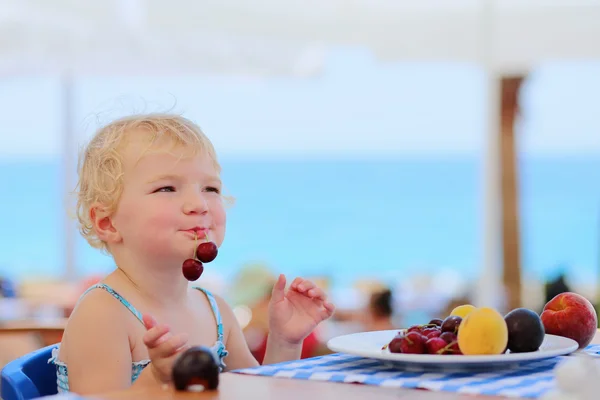 Gelukkig meisje eten fruit als dessert in restaurant aan het strand — Stockfoto