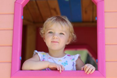 Happy little girl having fun in playhouse on a summer day clipart