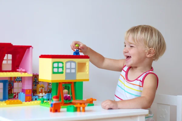 Glückliches kleines Mädchen baut Haus aus bunten Plastikklötzen — Stockfoto