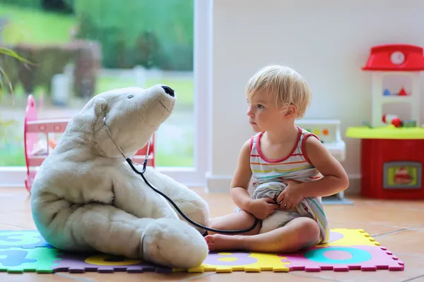 Little girl plays doctor providing healthcare to teddy bear — Stock Photo, Image