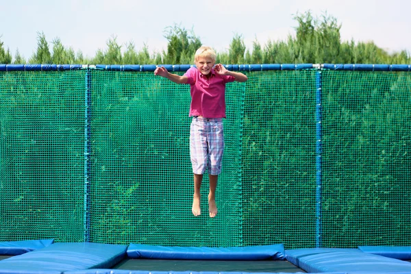 Glad skola pojke hoppar på studsmatta — Stockfoto