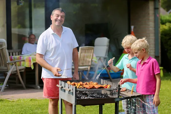 Father with kids preparing meat on barbecue in the garden — Stock Photo, Image