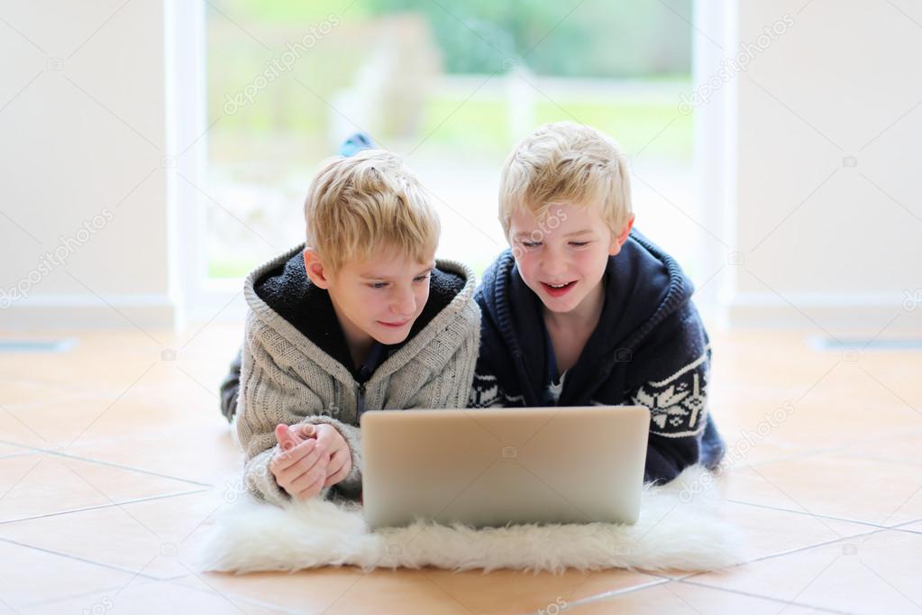 Two school boys working with laptop lying on the floor