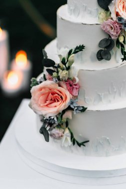 A wedding cake. Appetizing white cake four tiers on a beige table, decorated with roses, eucalyptus, light green background