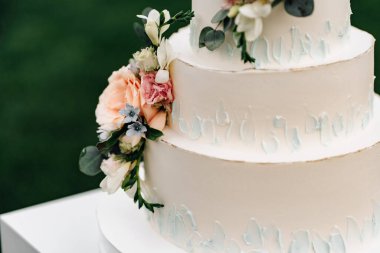 A wedding cake. Appetizing white cake four tiers on a beige table, decorated with roses, eucalyptus, light green background