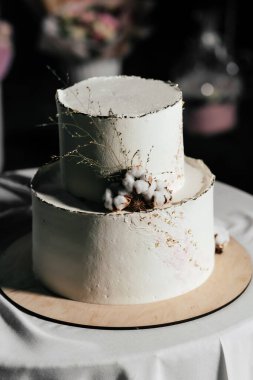 Düğün pastası. Pamuk boncuklarla süslenmiş süt renkli pasta ve arka planda altın yaprak.