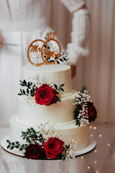 A wedding cake. Three tier cake with wedding rings decorated with red roses