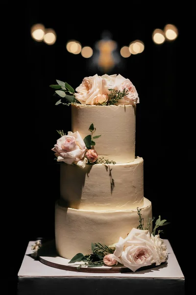 Düğün pastası. Kek bej bir masada üç katlı, güllerle süslenmiş koyu arkaplan