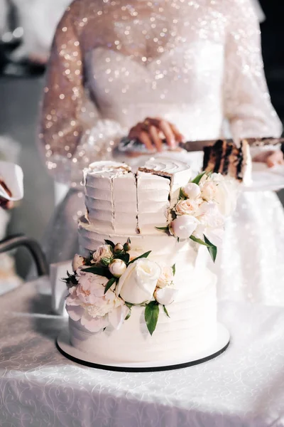 Düğün pastasını kesiyorum. Düğün pastası. İştah açıcı pasta bej bir masada üç kat, güllerle süslenmiş hafif bir arkaplan