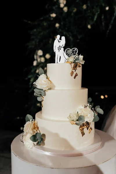 结婚蛋糕 米色桌子上的三层蛋糕 装饰过的玫瑰 深色背景上的金叶 — 图库照片