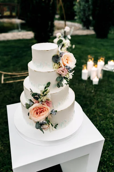 A wedding cake. Appetizing white cake four tiers on a beige table, decorated with roses, eucalyptus, light green background