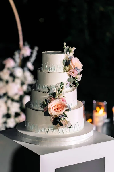 A wedding cake. Appetizing white cake four tiers on a beige table, decorated with roses, eucalyptus, light green background