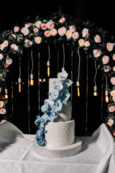 Düğün pastası. Şekerler. Düğün pastası siyah zemin üzerinde üç kat beyaz mastik süslemeli düğün günü mastikten mavi ve mavi orkidelerle süslenmiş.