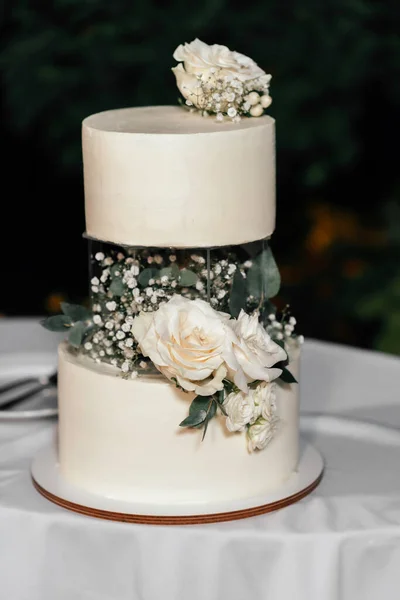 Düğün pastası. Güzel bir cam dekorlu sütlü pasta koyu arkaplanda güller, okaliptüsler ve çiçeklerle süslenir.