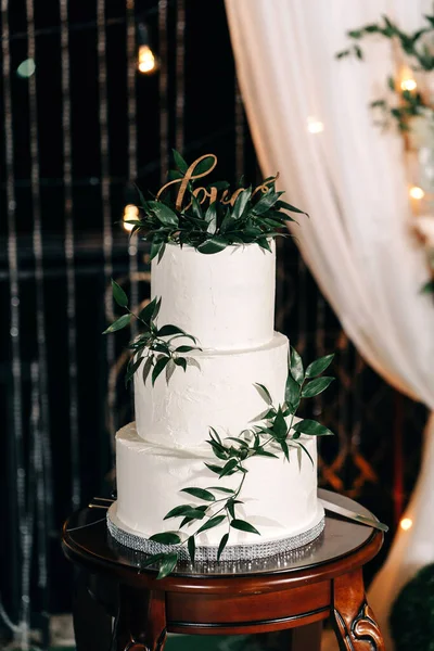 Üç kat beyaz düğün pastası. Üstünde beyaz mastik krem ve şifalı otlarla süslenmiş.