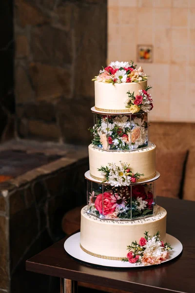 wedding cake three floors with white mastic decorated with different flowers of rose chamomile on the background of cozy home