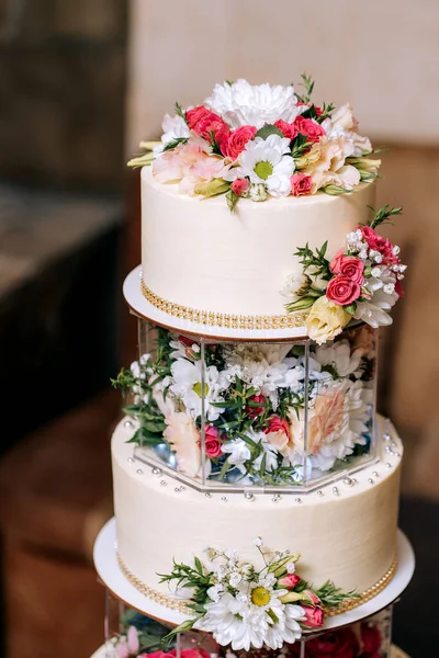wedding cake three floors with white mastic decorated with different flowersrose chamomile on the background of a cozy home