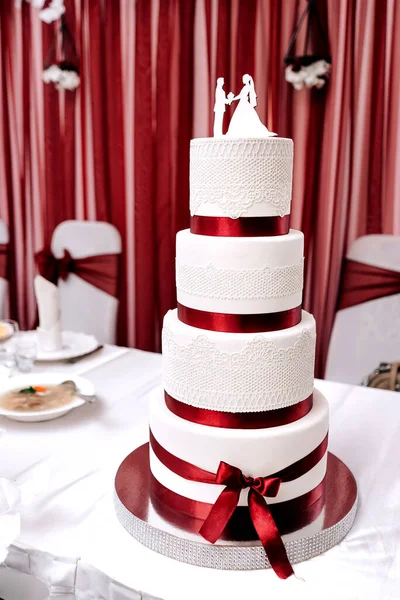 wedding cake white cream mastic four floors with red ribbons bow with newlyweds from above white background