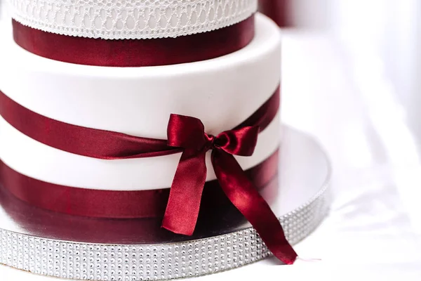 wedding cake white cream mastic four floors with red ribbons bow with newlyweds from above white background