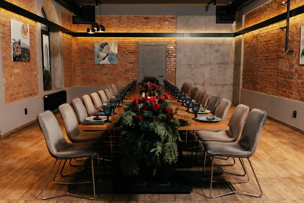 Çatı katı tarzı bir restoranda gözlüklerle servis edilen uzun bir masa, sıcak ışıklandırmalı tabaklar ve tablolarla servis edilir.