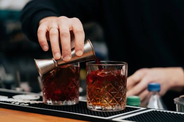 İşteki barmen iki kişilik buzlu bardağa alkollü içecek doldurur.