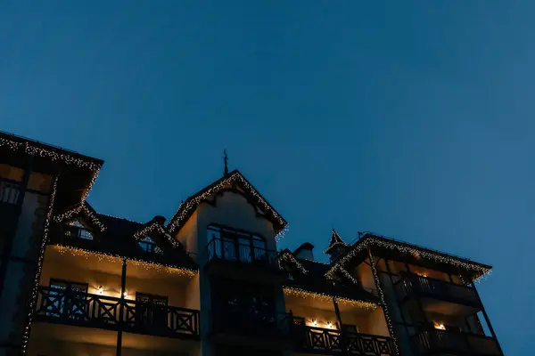 Ev geceleri duruyor, gökyüzüne karşı çelenk ve sıcak lambalarla aydınlanıyor.