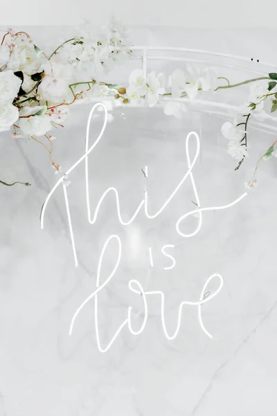 Yazıt - bu aşk. Düğün günü beyaz zemin üzerinde beyaz renkli neon yazıtlar ve çiçekler..