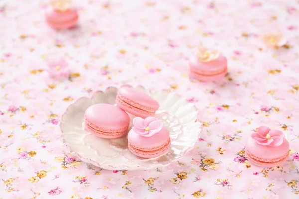 Macarons roses sur assiettes blanches, sur une nappe florale rose clair — Photo