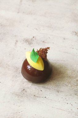 Çağdaş çikolatalı Mousse Dome Kekleri, çikolata aynası jöleli ve sarı kadife kaplama limonlu kremayla kaplı, yeşil çikolata yaprakları ve açık arkaplanda yosun süngeriyle süslenmiş..