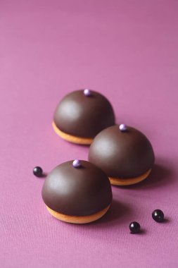 Mini Dome Pastaları - Ptichye Moloko (Kuş Sütü) - Geleneksel Rus Sufle Pastası, siyah frenk üzümü ile kaplı, çikolata jöleli ve şeker toplarıyla süslenmiş, mor arka planda.