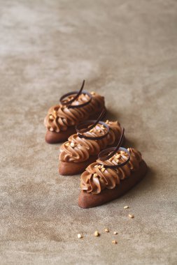Çikolata Kahveli Çörek Kurabiyeleri Fıstıklı Praline ve Kremalı Çikolatalı Kahve Kreması, çikolata sarmalı, açık kahverengi kadife arka planda.
