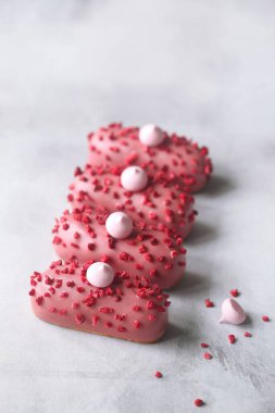 Pink Eclair with Raspberry Cream Filling, covered with pink chocolate and sprinkled with freeze-dried raspberries, on light grey background.