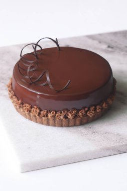 Çağdaş Çikolatalı Praline Kremalı Kek, çikolata aynası jölesiyle kaplı ve çikolata spiralleriyle süslenmiş, açık gri mermer tahtada..