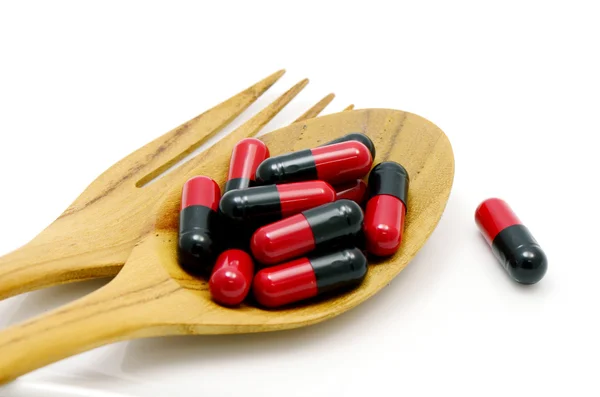 Oral medication red and black capsules in a table spoon on white background. — Stock Photo, Image